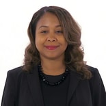 A person with long, wavy hair in a black blazer and necklace smiles against a plain white background, reflecting Medbridge's professional ethos.