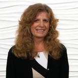 A woman with long curly hair and a black and white outfit smiles in front of a textured white background, representing medbridge innovation.