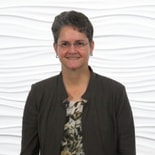 A smiling person with gray hair and glasses stands confidently, embodying their role in healthcare training and medbridge software innovation.