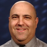 A smiling bald man in a gray shirt and tie represents Medbridge's vision for digital healthcare.