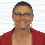 A smiling person with short hair and glasses wearing a red top is in front of a wavy white background.