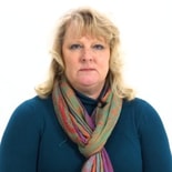 A blonde woman in a blue top and multicolored scarf against a white background, embodying healthcare dedication.