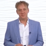 A person wearing a blue blazer and white shirt stands before a white textured background.