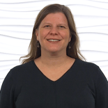 A smiling person with long hair in a black top stands against a textured white background, capturing the positivity of medbridge healthcare training.
