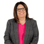 Woman with brown hair, glasses, and a grey blazer smiles, representing medbridge's digital healthcare and hybrid care professionalism.