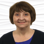 A smiling woman in a purple top and black cardigan stands against a wave-patterned wall, representing Medbridge in digital healthcare.
