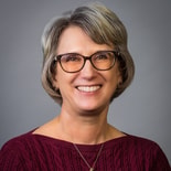 A woman in a maroon sweater and glasses smiles warmly, reflecting healthcare education expertise, featured in medbridge content.