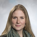 A confident individual with long blonde hair wears a patterned scarf and earrings, reminiscent of a medbridge software expert.