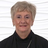A confident person with short light hair modeling expertise in patient care software, against a white background.