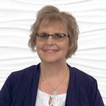 A woman with glasses and short blonde hair in a navy blazer smiles confidently, reflecting her expertise at medbridge in hybrid care solutions.