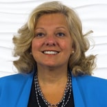 A smiling woman with wavy blonde hair, in a blue blazer and pearl necklace, represents Medbridge's healthcare education.