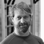 A man in a long-sleeve shirt stands indoors, embodying digital healthcare advancements, in a black-and-white image for medbridge.