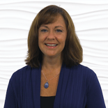 Person smiling in a dark blue cardigan and necklace against a textured white background for medbridge.