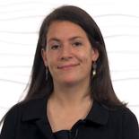 A woman with long dark hair smiles warmly, embodying her passion for healthcare training, in front of a wavy white background.