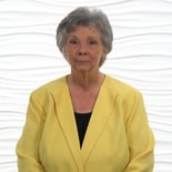 A woman in a yellow jacket stands against a wavy white backdrop at a medbridge healthcare training event.