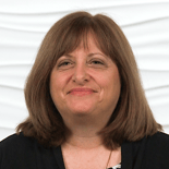 A woman with brown hair in a black top smiles against a white textured background.