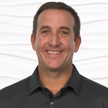 A person in a dark polo shirt smiles against a wavy white background.