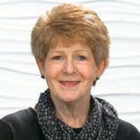 A person with short light brown hair smiles, wearing a black top and polka dot scarf, against a white textured background akin to medbridge's seamless integration in digital healthcare.
