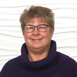 A smiling individual with glasses and short hair stands against a white wavy background, embodying healthcare education expertise for medbridge.