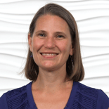 A woman with short brown hair in a dark blue blouse smiles warmly, embodying the modern professionalism of medbridge's digital healthcare advancements.