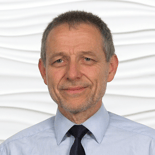 A bearded man in a light blue shirt and dark tie stands before a white wall, symbolizing digital healthcare innovation at medbridge.
