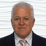 An older man with white hair in a suit and tie smiles against a textured white background.