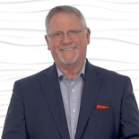 A smiling man with glasses and a grey beard in a navy suit with an orange pocket square, against a backdrop reflecting digital healthcare advances for medbridge.