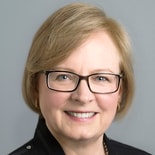 A smiling person with short hair and glasses, wearing a black top, represents medbridge's healthcare education spirit.