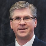 Man with glasses and gray hair in a suit and tie, representing professionalism for medbridge in digital healthcare.
