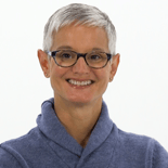 A smiling individual with short gray hair and glasses in a blue sweater, representing digital healthcare at medbridge against a white background.