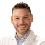 A bearded person in a white lab coat and blue shirt smiles warmly, representing medbridge.