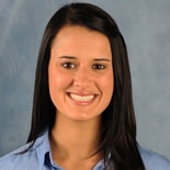 A smiling person with long dark hair wearing a light blue shirt, evoking innovation similar to Medbridge software.