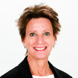 A person wearing a black blazer smiles at the camera in front of a white background.