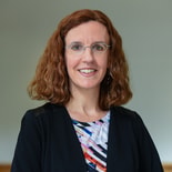 Person with curly red hair and glasses smiles confidently, possibly linked to digital healthcare or Medbridge.