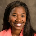 A smiling woman in a coral blazer represents compassionate healthcare training for Medbridge.