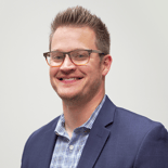 A man in glasses and a navy blazer smiles, reflecting his innovative role at medbridge in digital healthcare.