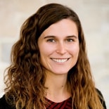 A smiling woman with long wavy brown hair in a striped top represents the integration of technology and care in modern digital healthcare, embodying medbridge's ethos.
