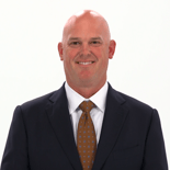 A bald man in a dark suit and polka dot tie smiles, representing medbridge's digital healthcare professionalism.
