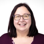Woman with straight dark hair, glasses, and a maroon top smiles at the camera against a white background.