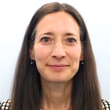 A woman with long brown hair and earrings smiles subtly, illustrating hybrid care in a medbridge setting.
