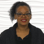 Curly-haired person with glasses in dark top, smiling against a textured white background for medbridge.