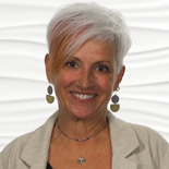 A smiling woman with short, colorful hair and dangling earrings wears a beige blazer in front of a white textured background for medbridge.