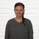 A woman in a gray sweater and long earrings smiles warmly, embodying dedication to healthcare training with medbridge.