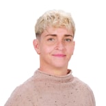 A smiling person with short curly blonde hair and earrings wears a light brown textured sweater, embodying the warmth of medbridge patient care software.