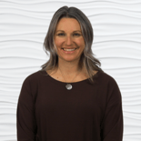 A woman in a dark top smiling warmly, representing compassionate care and innovative healthcare training for medbridge.