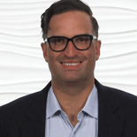 A smiling person with glasses in a blazer and shirt, representing medbridge's professional yet approachable digital healthcare image.