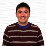A smiling person in a maroon and white striped sweater stands before a healthcare-themed backdrop, reflecting medbridge training.