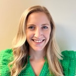 A smiling woman with long blonde hair in a green top stands against a light wall, embodying the positive impact of hybrid care highlighted by medbridge.