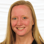A smiling woman with long blond hair in a black top stands against a white background for medbridge.