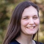A smiling person with long brown hair stands outdoors, embodying healthcare education with medbridge.